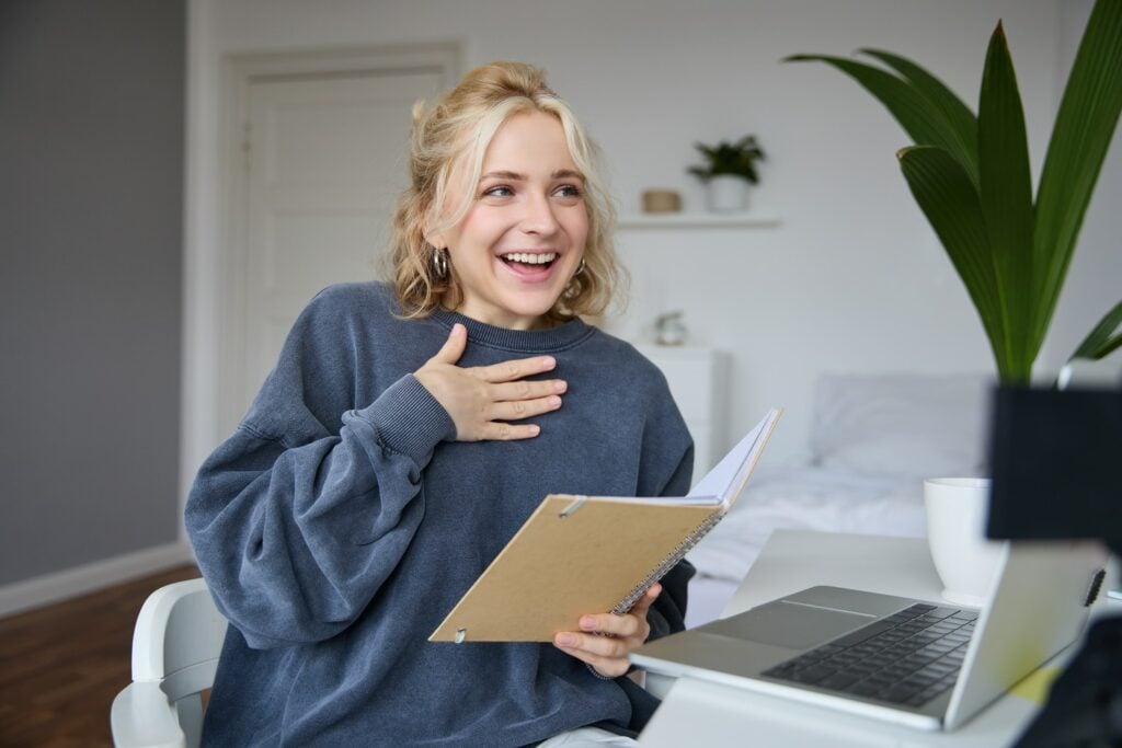 chica rubia sonrie mientras sostiene un cuaderno